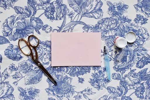 Twelve inch paper trimmer in cream and copper with a swing-out measuring arm extended, a printed inch grid on the base and a 12x12 patterned sheet aligned under the blade rail